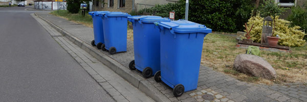 Vier blaue Papiertonnen am Straßenrand
