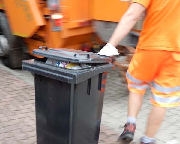 Foto: Ein Müllwerker zieht einem Restabfallbehälter zum Sammelfahrzeug